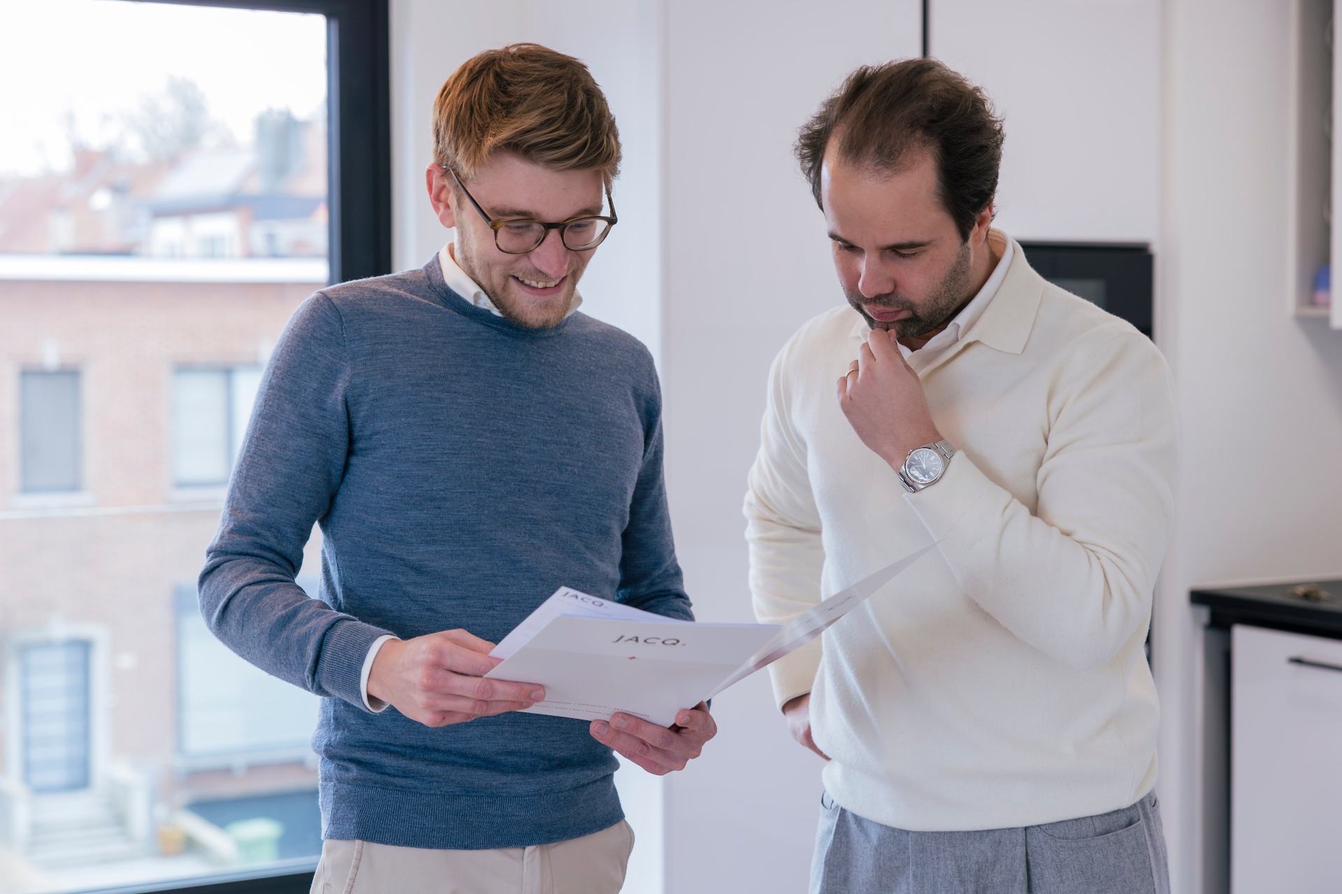 Twee JACQ-collega's bekijken samen een vastgoedbrochure in het kantoor